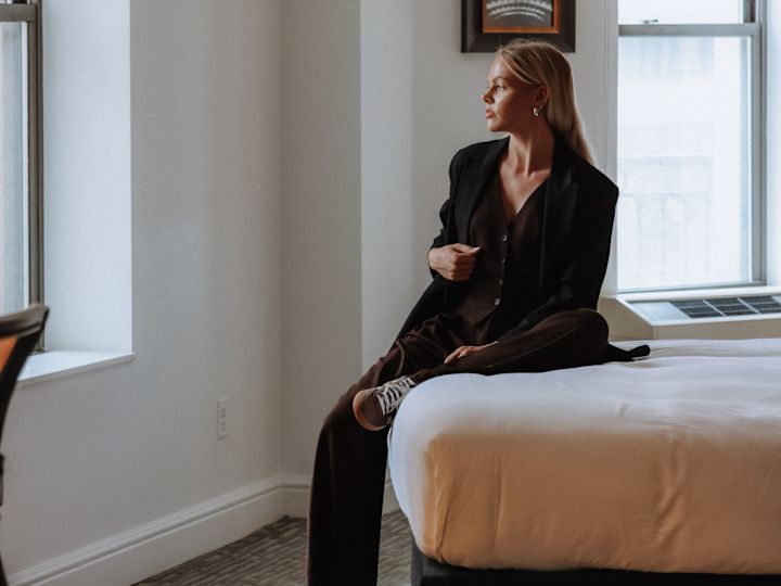 Woman Wearing a Black Suit Sitting on a Bed in a Guest room