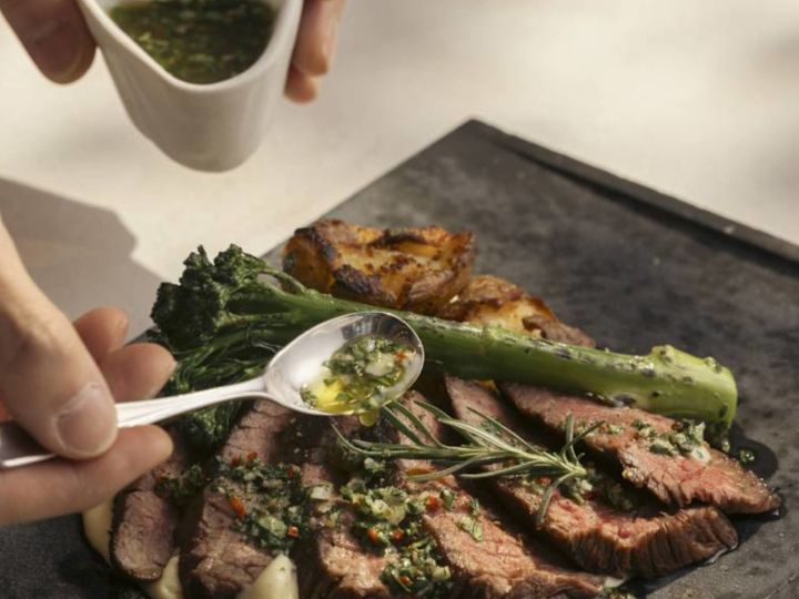 Person Adding Sauce to a Meat Dish