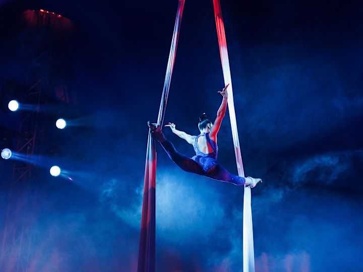 Frau, die Luftakrobatik durchführt und durch Farbbänder von der Luft hängen lässt