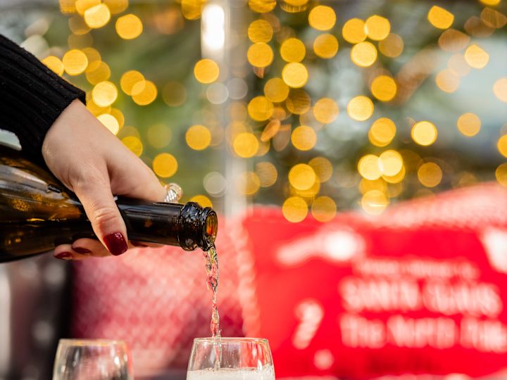 Woman Pouring Champagne into a Glass on a Table with Snacks on a Tray