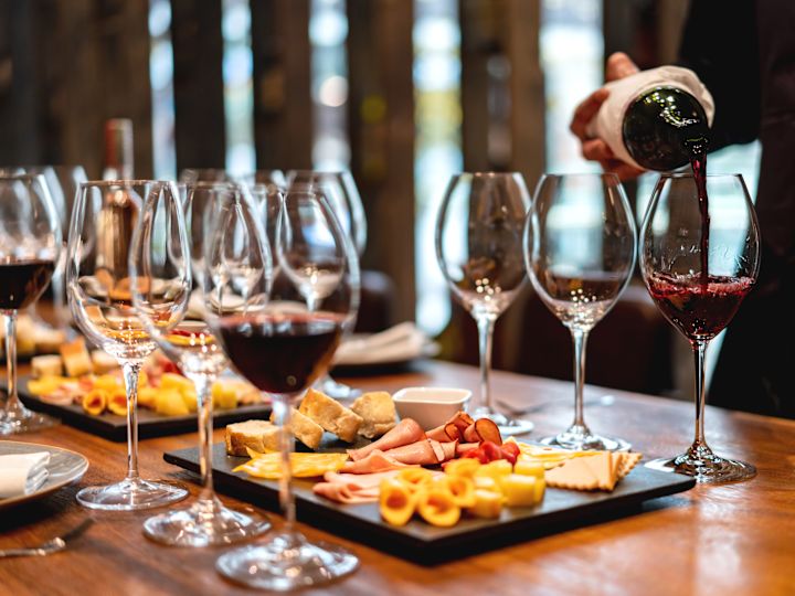 Person Pouring Wine in a Glass on a Table with Snacks for Wine Tasting