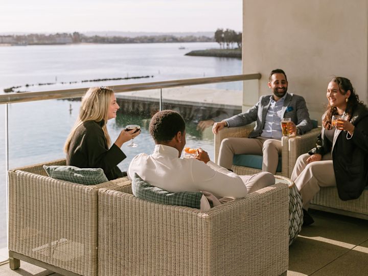 Four adults sitting on the terrace having drinks with the bay in the background while staying at the hotel during a team building event.