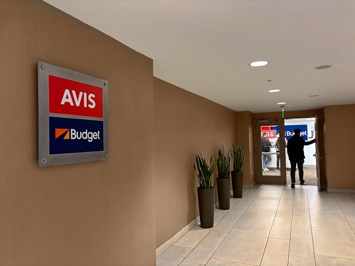 Duvardaki Avis ve Budget Logoları ve Araba Kiralamaya Giren Bir Adam