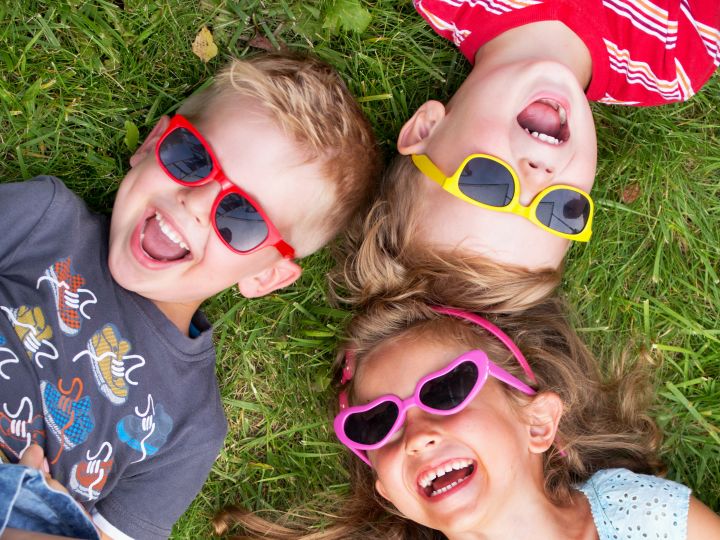 Three children lying on the grass laughing with sunglasses on.