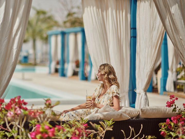 Femme assise près de la piscine dans une cabana avec une boisson