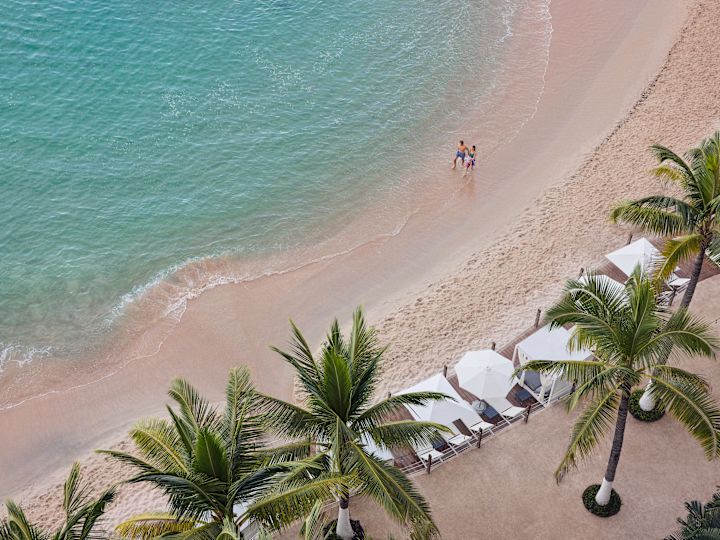 ヤシの木やカバナを通り過ぎてビーチを歩く男女