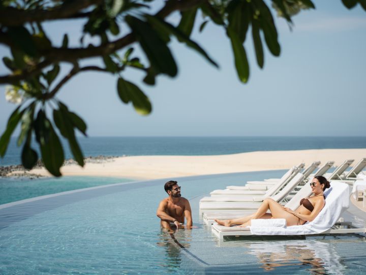 couple lounging at infinity pool overlooking beach