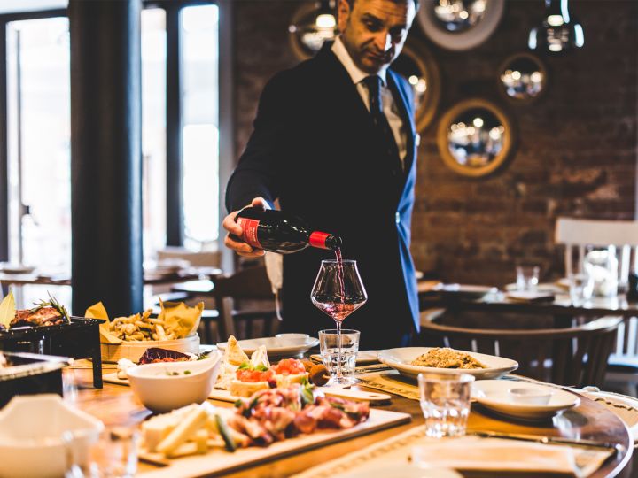 waiter pouring wine at table with food