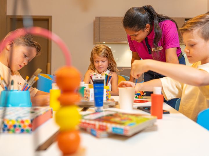 Kids doing arts and crafts with adult woman supervising