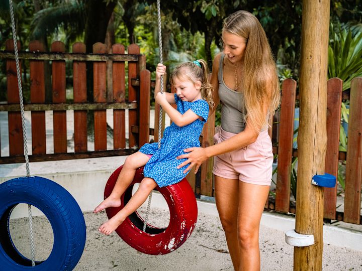 a woman and a girl playing on a tire swing outdoors