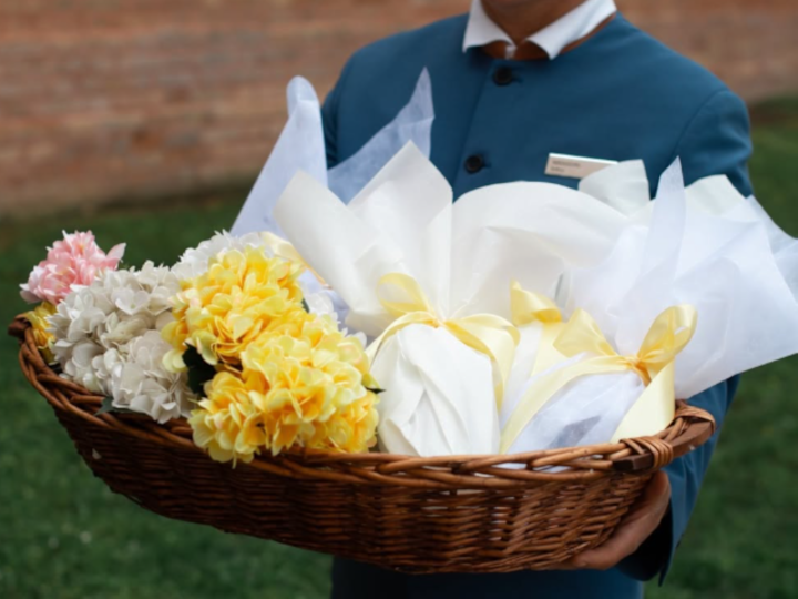 Person Holding a Basket with Flowers and Gifts Wrapped with a Yellow Bow