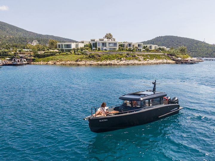 Bir Tekne Yolculuğunun Keyfini Çıkaran İnsanlar ve Arka Planda Susona Bodrum Otel’in Görünümü