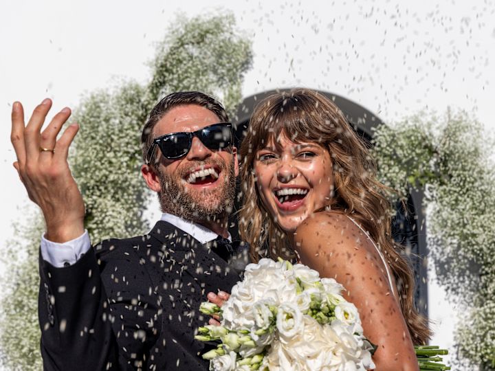 Mann und Frau in Hochzeitskleidung lächeln, während Konfetti um sie herumfällt