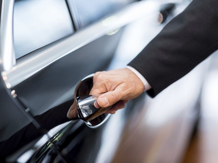 Uomo che indossa abiti formali con la mano sulla maniglia di una porta dell'auto