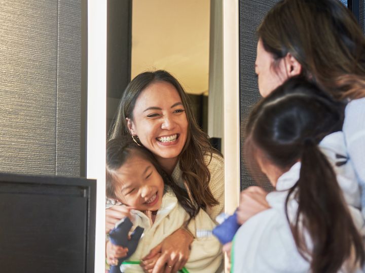 Mother and Daughter Wearing Robes, Looking in a Mirror in a Guest Room
