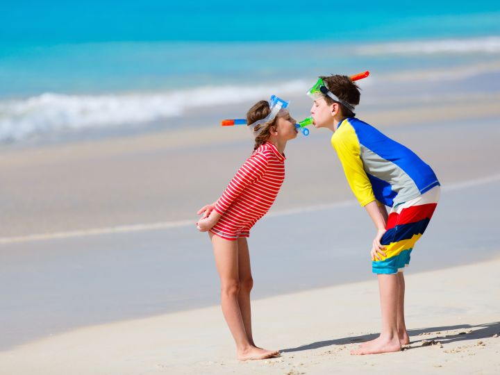 Little kids in rash guards for sun protection with snorkeling equipment on tropical beach having fun during summer vacation