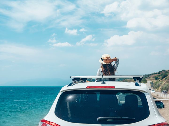 Woman standing in car sunroof overlooking ocean