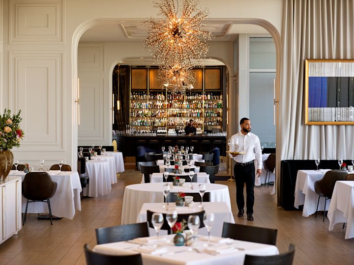 Staff member in white shirt walking through restaurant area with tables and chairs