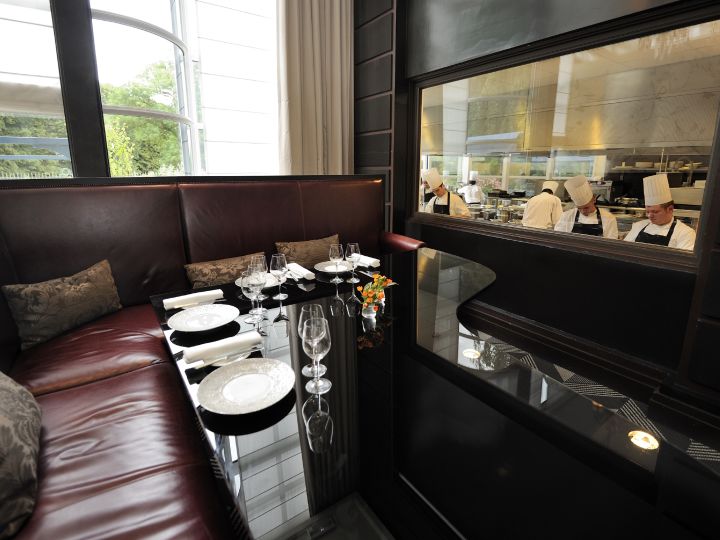 Essbereich und Blick auf die Köche, die im Restaurant "Gordon Ramsay au Trianon" Speisen zubereiten