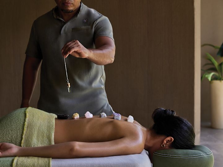 Woman on massage table with masseuse applying rocks