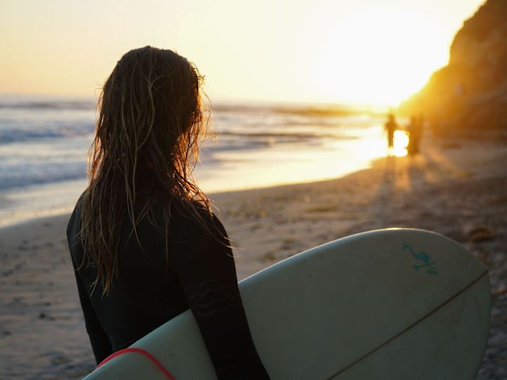Woman admiring the sunrise on the beach holding a surfboard