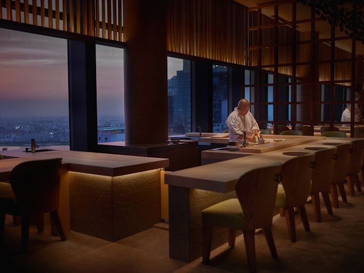 Tsukimi chef preparing for service with a view of the city at sunset behind him.