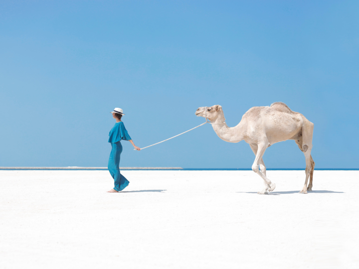 a lady leading a camel in the desert