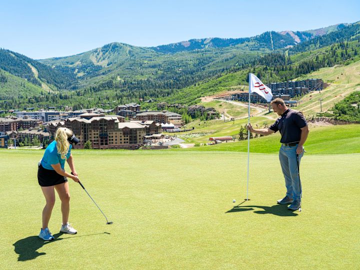 Man and woman on putting green. The man is holding the flag