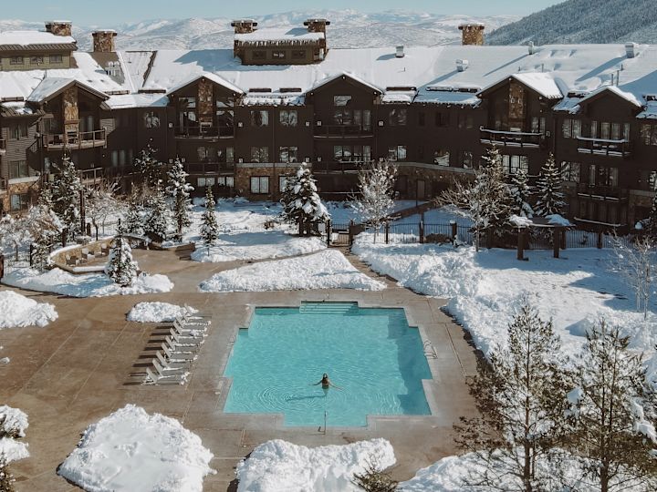 Femeie într-o piscină exterioară într-o zi de iarnă înzăpezită, cu vedere spre exterior spre hotel