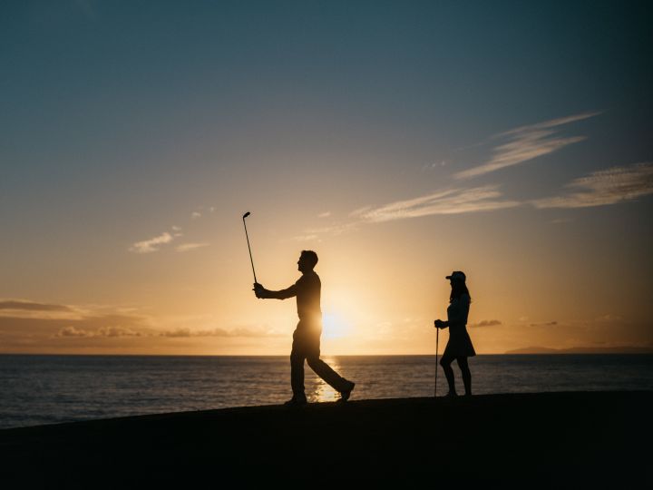 a couple playing golf next to a beach at sunset
