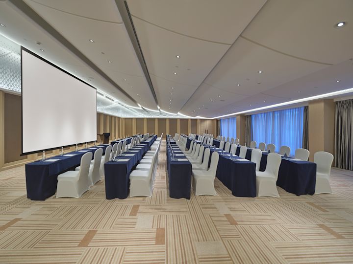 Sala konferencyjna ze stołami i krzesłami skierowanymi w stronę dużego ekranu projektora