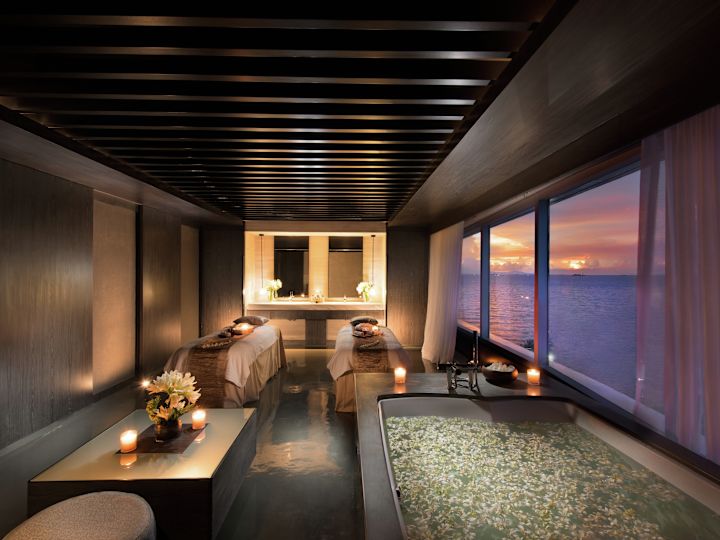 Une magnifique salle de soins de spa avec une grande fenêtre surplombant l'océan au coucher du soleil.