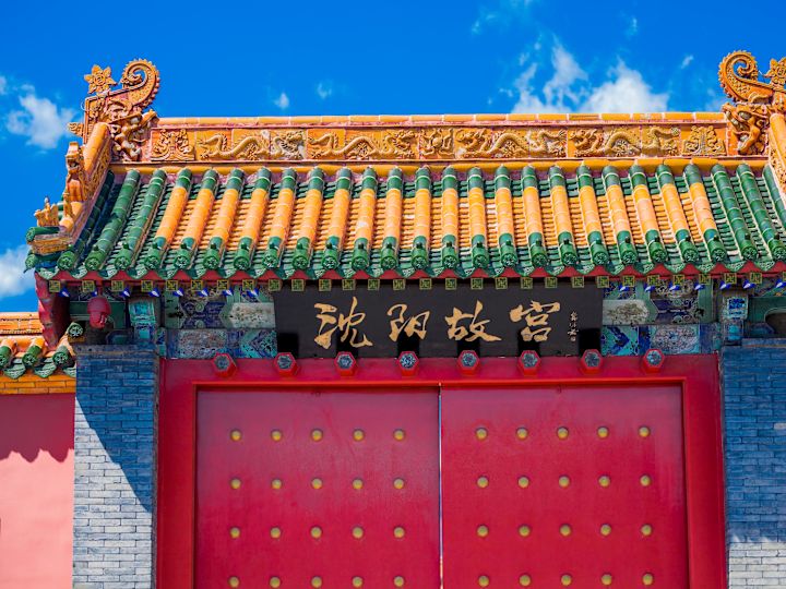 Traditionelles chinesisches Palasttor mit roten Nietentüren, geschnitzten Dachdetails und einer goldfarbenen Plakette mit dem Shenyang Imperial Palace.