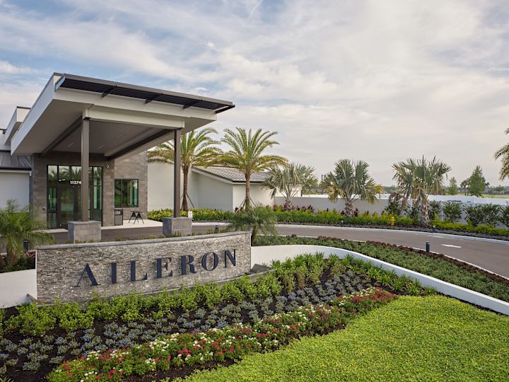 Pintu Masuk Lapangan Golf Aileron dengan Papan Tanda, Bunga, dan Pohon Kelapa Sawit