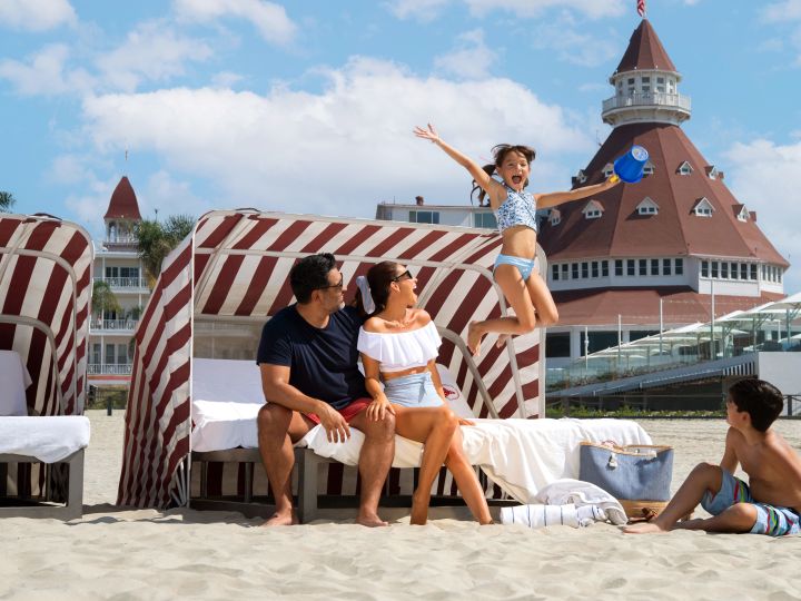 Family sitting in a cabana on the beach with hotel in the background