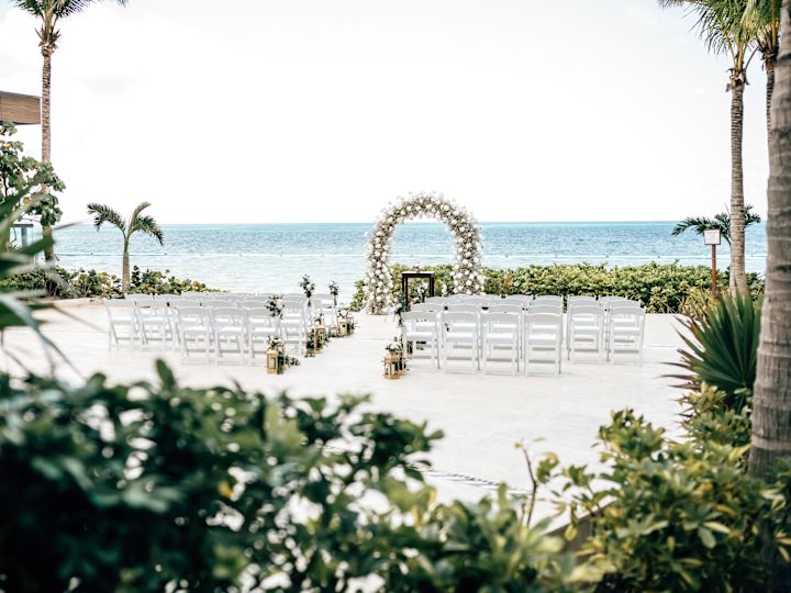 beach wedding ceremony set up with chairs and a flower arch