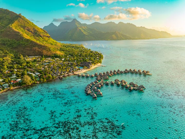 Vue aérienne du Hilton Moorea Lagoon Resort & Spa avec des bungalows sur l'eau et les montagnes en arrière-plan