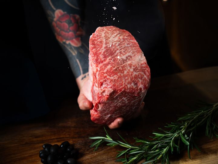 Chef ținând o bucată de carne neprelucrată la restaurantul OXBO Bangkok