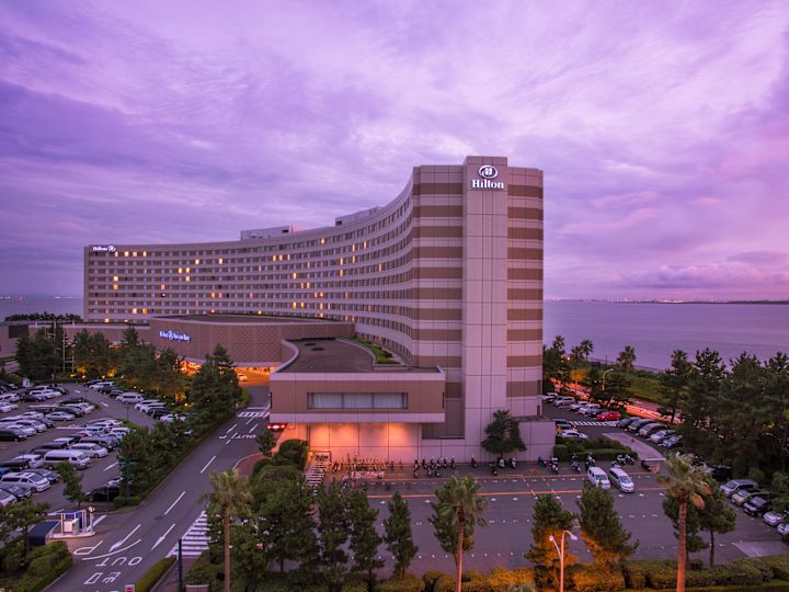 Illuminated Hotel Exterior, Signage, and Guest Cars on Parking Lot at Dusk