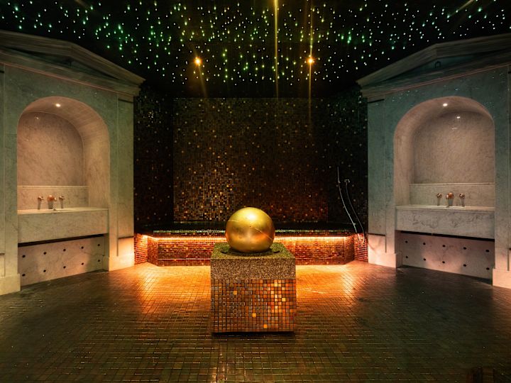 O cameră spa de lux, slab luminată, cu pereți de mozaic întunecat și un tavan proiectat pentru a arăta ca o noapte înstelată