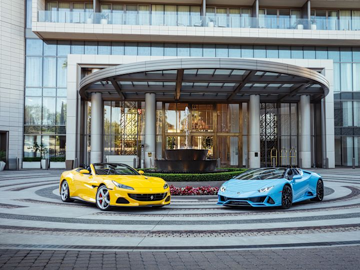 酒店外观，建筑前有黄色和蓝色的车以及喷水池