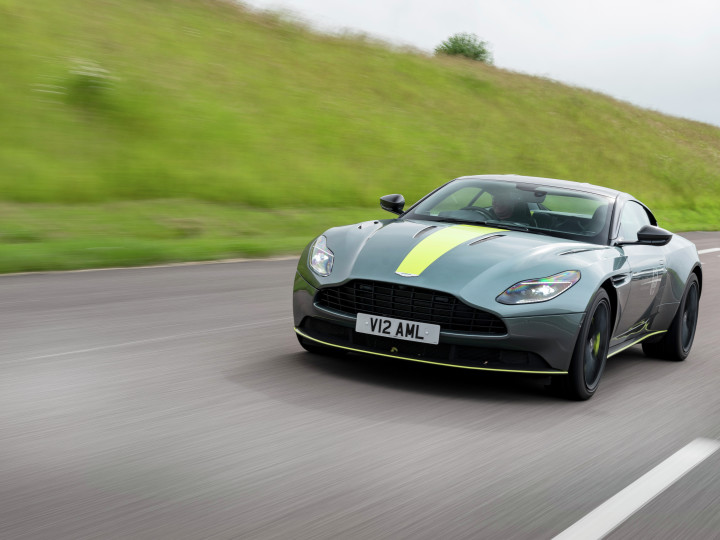 Aston Martin front view, on the road adjacent a green hill