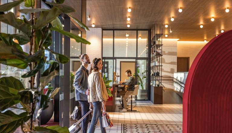 Hombre y mujer caminando por la entrada principal al lobby con equipaje
