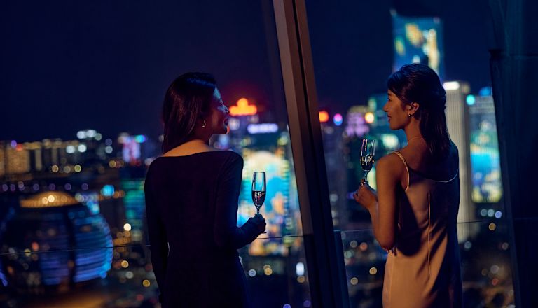 窓から市街の眺めを眺めながらグラスを手にする2人の女性