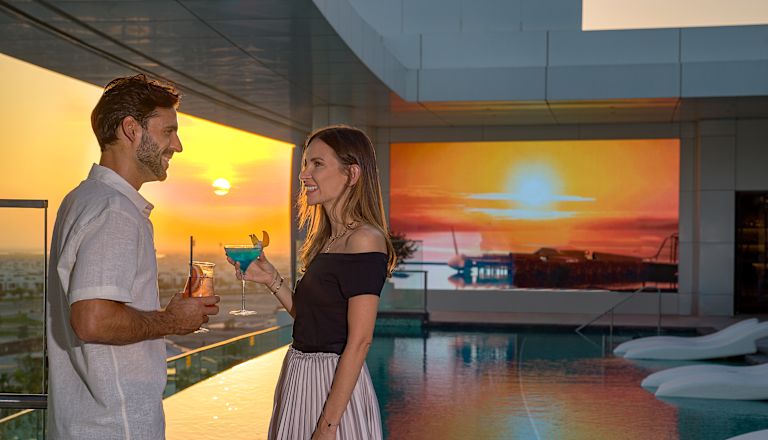 Mann und Frau bei Sonnenuntergang mit Drinks in der Nähe des Balkons