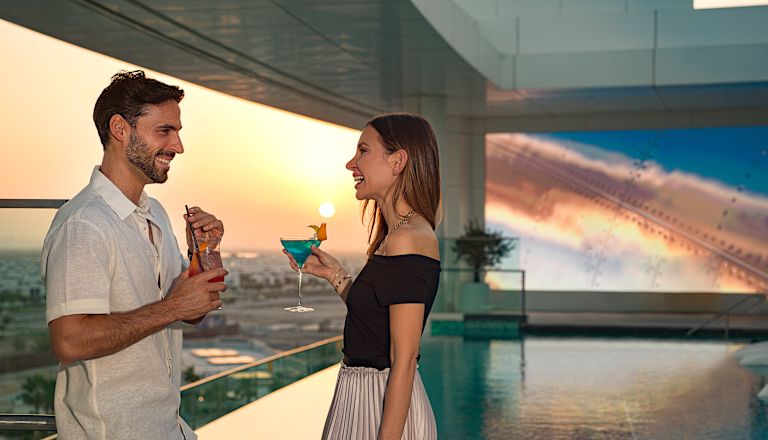 Mann und Frau mit Drinks in der Nähe des Balkons bei Sonnenuntergang