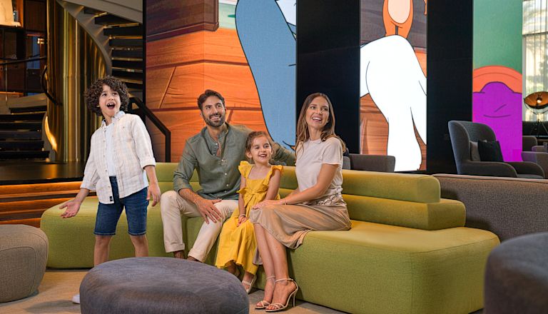 Familie auf grünem Sofa in der Lobby mit Wandbildern von Tom und Jerry