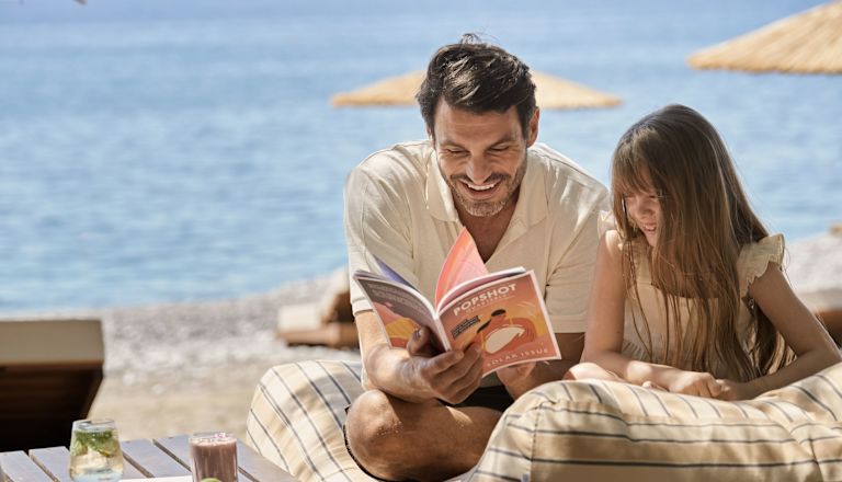 Father and Daughter Reading a Book and Snacking on Fruits at the Beach