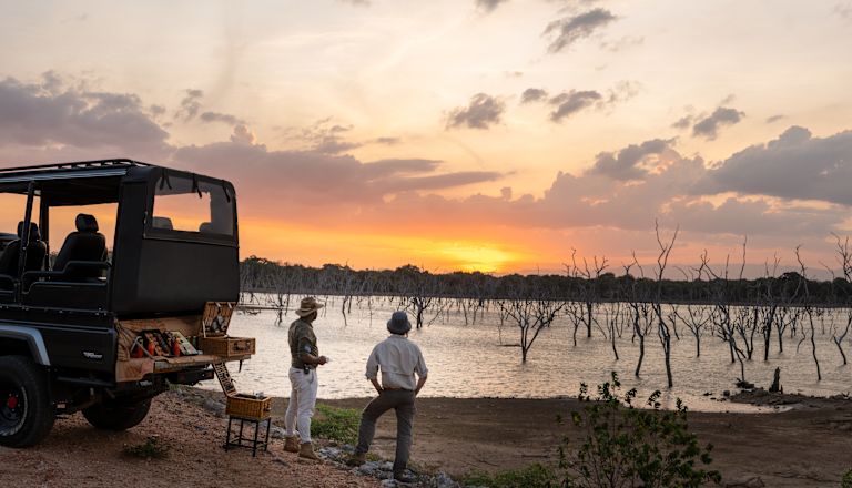 Wide shot of people on safari next to jeep