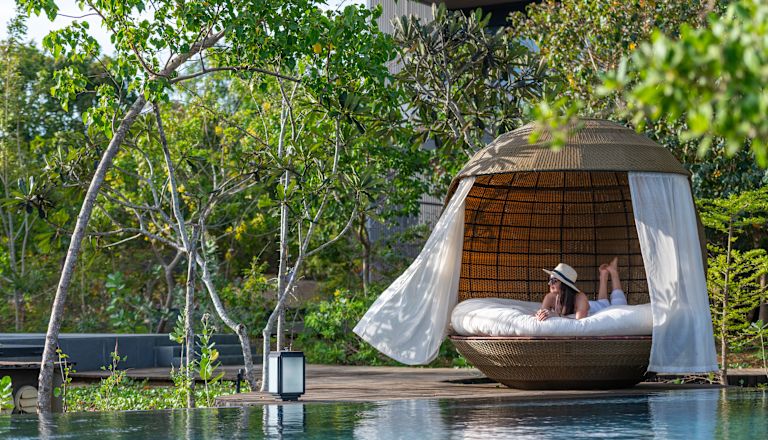 Person in pool lounge large wicker seating next to pool
